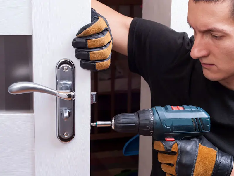 Man repairing door lock with electric drill.