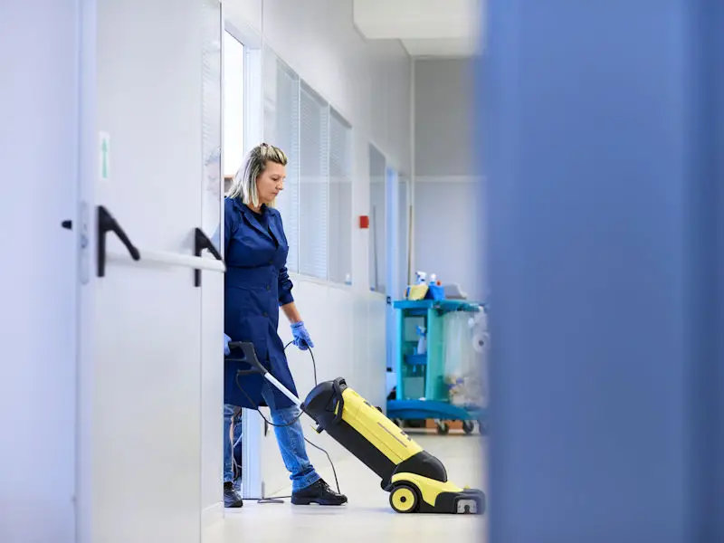 Woman cleaning office floor with vacuum cleaner.